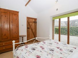 A bedroom with a wooden wardrobe, small round table, wooden door, bed with floral bedspread, and large window with green blind at Mistletoe Cottage in Kemeys Commander near Usk