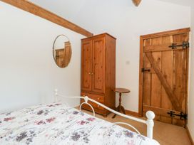 A bedroom with a floral bedspread a wooden wardrobe a small round table a wooden door and an oval mirror at Mistletoe Cottage in Kemeys Commander near Usk
