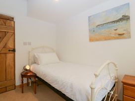 A bedroom with a single bed bedside tables a round wooden table with a lamp a wooden door and a painting on the wall at Mistletoe Cottage in Kemeys Commander near Usk