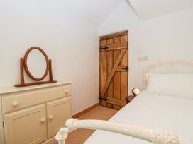A bedroom with a wooden door cream dresser with mirror and white bed at Mistletoe Cottage Kemeys Commander near Usk