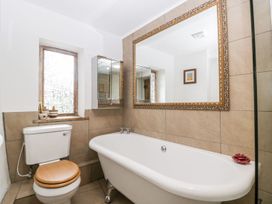 A bathroom with a toilet with wooden seat a white bathtub a large decorative mirror and a window with small potted plants at Mistletoe Cottage in Kemeys Commander near Usk