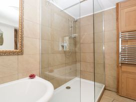 A bathroom with a shower enclosure a bathtub with a flower on the edge a mirror with a decorative frame and a heated towel rail at Mistletoe Cottage in Kemeys Commander near Usk