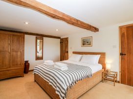 A bedroom with a bed with a striped blanket a wooden wardrobe a mirror and wooden doors at Mistletoe Cottage in Kemeys Commander near Usk