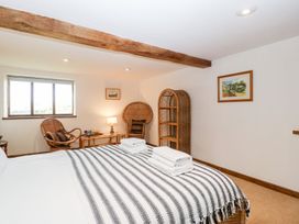 A bedroom with a bed, striped blanket, wooden beams, wicker chairs, and paintings on white walls at Mistletoe Cottage in Kemeys Commander near Usk