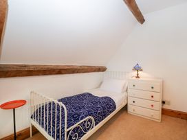 A bedroom with a single bed covered with a patterned blue blanket a white chest of drawers with a lamp and a small round side table at Mistletoe Cottage in Kemeys Commander near Usk