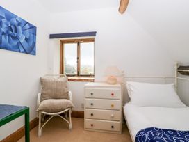 A bedroom with a white bed a colorful knob dresser a chair with cushions a window and a blue painting on the wall at Mistletoe Cottage in Kemeys Commander near Usk