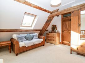 A sitting area with a wicker sofa and cushions a wooden dresser with a mirror and a wooden wardrobe in an attic room with exposed wooden beams and a skylight window at Mistletoe Cottage in Kemeys Commander near Usk