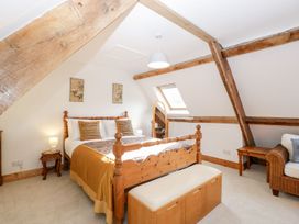 A bedroom with a wooden bed frame cushions and a blanket a bench a wicker armchair a side table and a full-length mirror at Mistletoe Cottage in Kemeys Commander near Usk