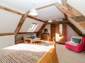 A bedroom with a wooden bed a wicker sofa a wooden wardrobe a chest of drawers and a pink armchair at Mistletoe Cottage in Kemeys Commander near Usk