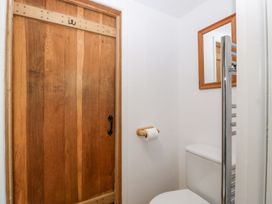 A small bathroom with a wooden door a toilet paper holder a white toilet a wall-mounted mirror and a chrome towel rail at Mistletoe Cottage in Kemeys Commander near Usk