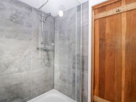 A shower area with gray tiled walls a glass shower screen and a wooden door at Mistletoe Cottage in Kemeys Commander near Usk