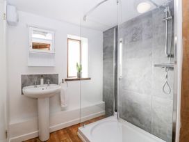 A bathroom with a pedestal sink a mirror cabinet a window with a plant and a shower with grey tiles at Mistletoe Cottage in Kemeys Commander near Usk