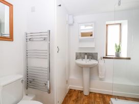 A bathroom with a toilet, pedestal sink, wall-mounted mirror cabinet, towel rack, potted plant on the window sill, and wooden floor at Mistletoe Cottage in Kemeys Commander near Usk