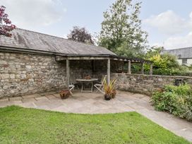 An outdoor covered seating area with stone walls a wooden table and chairs potted plants on a stone patio at Mistletoe Cottage in Kemeys Commander near Usk