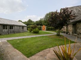 A garden with stone pathways shrubs a wooden shed and a stone building at Mistletoe Cottage Kemeys Commander near Usk