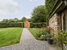 A garden with a gravel path leading to a wooden gate stone wall of a house and flower plants at Mistletoe Cottage in Kemeys Commander near Usk