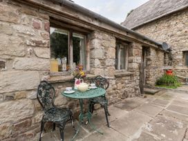 A stone-walled outdoor patio with two metal chairs and a round metal table with a teapot and cups at Mistletoe Cottage in Kemeys Commander near Usk