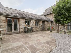 A stone patio with a small table and two chairs outside a stone house with wooden doors and windows at Mistletoe Cottage in Kemeys Commander near Usk