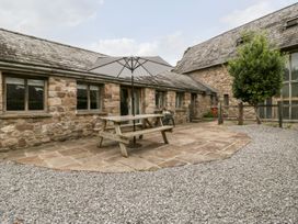 An outdoor patio area with a wooden picnic table and umbrella outside a stone building at Mistletoe Cottage in Kemeys Commander near Usk