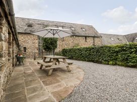An outdoor patio area with a wooden picnic table and umbrella alongside stone buildings and a hedge at Mistletoe Cottage in Kemeys Commander near Usk