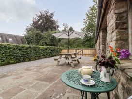 A patio with a green metal table holding a teapot cup and flowers and a wooden picnic table with an umbrella near a stone wall at Mistletoe Cottage in Kemeys Commander near Usk