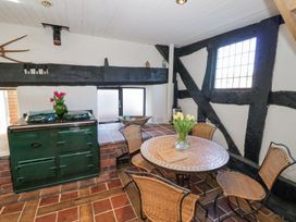 A kitchen area with a green stove a round tiled table with a vase of flowers and four wicker chairs at Wyre Court Cottage in Bewdley