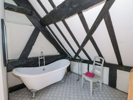 A bathroom with a clawfoot bathtub a wooden chair with a pink towel and exposed black wooden beams on the walls at Wyre Court Cottage in Bewdley