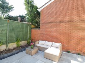 An outdoor patio with a wicker sofa and table with flowers against a brick wall and green fence at Wyre Court Cottage in Bewdley