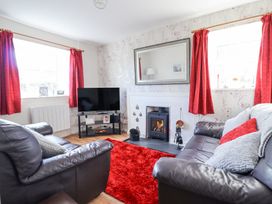 A living room with two leather sofas a red rug a wood burning stove and a television at Minffordd in Pandy Tudur near Betws-Y-Coed