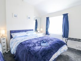 A bedroom with a double bed blue bedding two bedside tables with lamps blue curtains and a luggage rack near a window at Minffordd in Pandy Tudur near Betws-Y-Coed