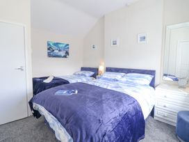 A bedroom with a double bed and a single bed with blue bedding a bedside table with a lamp a white dresser with a mirror and small stool and framed pictures on the wall at Minffordd in Pandy Tudur near Betws-Y-Coed
