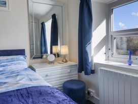 A bedroom with a bed, dresser with lamp and mirror, blue curtains, and a window with decorative items at Minffordd in Pandy Tudur near Betws-Y-Coed