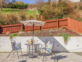 A patio with a table and four chairs under an umbrella with cushions on two chairs and a bottle with glasses on the table at Minffordd in Pandy Tudur near Betws-Y-Coed