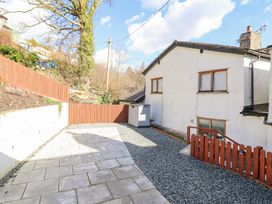 A paved patio and gravel area outside a white house with a wooden fence and storage shed at Minffordd in Pandy Tudur near Betws-Y-Coed