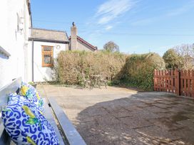 A paved outdoor patio with a metal bench with patterned cushions a small metal table with two chairs and a wooden gate with shrubs behind at Minffordd in Pandy Tudur near Betws-Y-Coed
