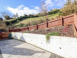 A paved outdoor area with a retaining wall and wooden fence on a sloping hillside at Minffordd in Pandy Tudur near Betws-Y-Coed