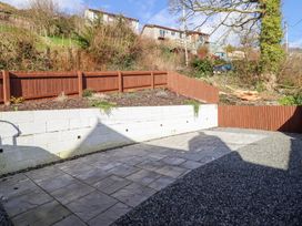 A paved and gravel backyard with a white retaining wall and brown wooden fences surrounding planted area at Minffordd in Pandy Tudur near Betws-Y-Coed