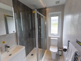 A bathroom with a shower, toilet, sink, and window at Dahlia in Portreath