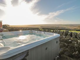 An outdoor hot tub near a stone wall with rolling hills in the background at Petty Knowes Cottage Rochester near Otterburn