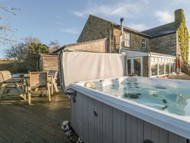 An outdoor patio with a hot tub and wooden table with chairs beside a stone house at Petty Knowes Cottage Rochester near Otterburn