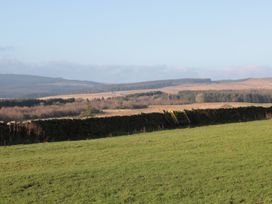 A grassy field with a stone wall and hills in the background at Petty Knowes Cottage Rochester near Otterburn
