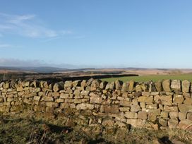 A stone wall with grassy fields and hills under a blue sky at Petty Knowes Cottage in Rochester near Otterburn