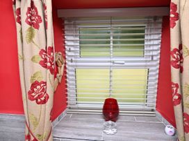 A window with curtains and a red vase at Petty Knowes Cottage Rochester near Otterburn
