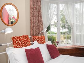 A bedroom with a bed with red and white pillows next to a window with white curtains and a round mirror on the wall at Alway in Lifton