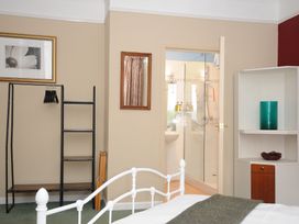 A bedroom with a white metal bed, open doorway to a bathroom with a glass shower, a black open wardrobe with hangers, a wall mirror, and a white corner shelf with a green vase at Alway in Lifton