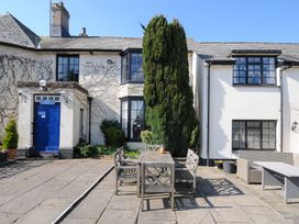 An outdoor patio area with wooden table and chairs in front of a white building with black window frames at Alway in Lifton