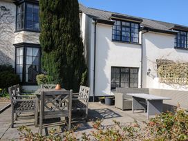 An outdoor patio area with wooden chairs and a table near a white house with black window frames at Alway in Lifton