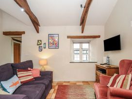 A living room with a purple sofa and a red armchair a wooden cabinet with a wall mounted TV and wooden ceiling beams at The Barn in Lifton