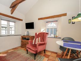 A sitting area with a pink armchair a wooden cabinet and a wall-mounted tv near windows and a table with chairs at The Barn in Lifton