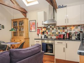 A kitchen with white cabinets a tiled backsplash and a wooden cabinet with books at The Barn in Lifton